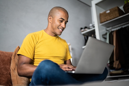 Man in yellow t-shirt sitting on sofa with laptop 
