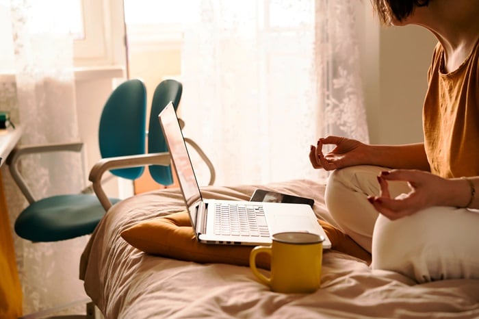 Lady looking at laptop crossed legged on bed in calming pose 