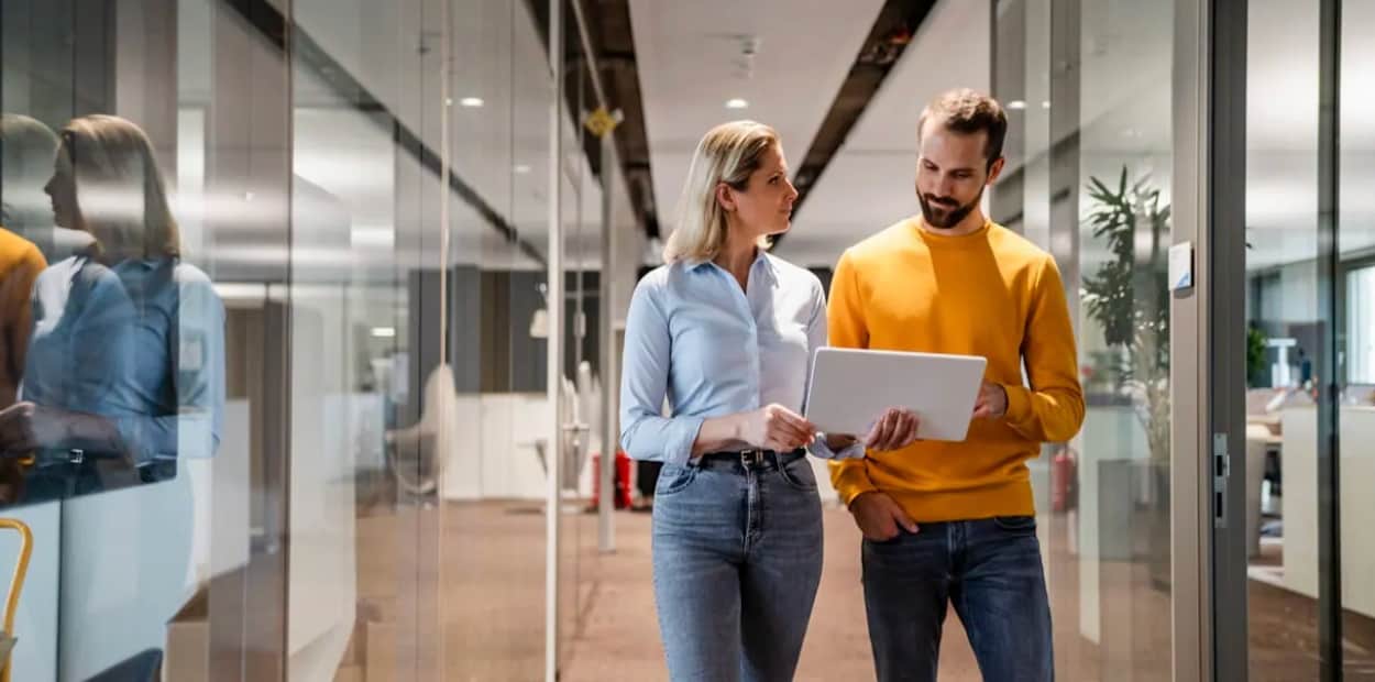 man and woman walking down office talking with ipad