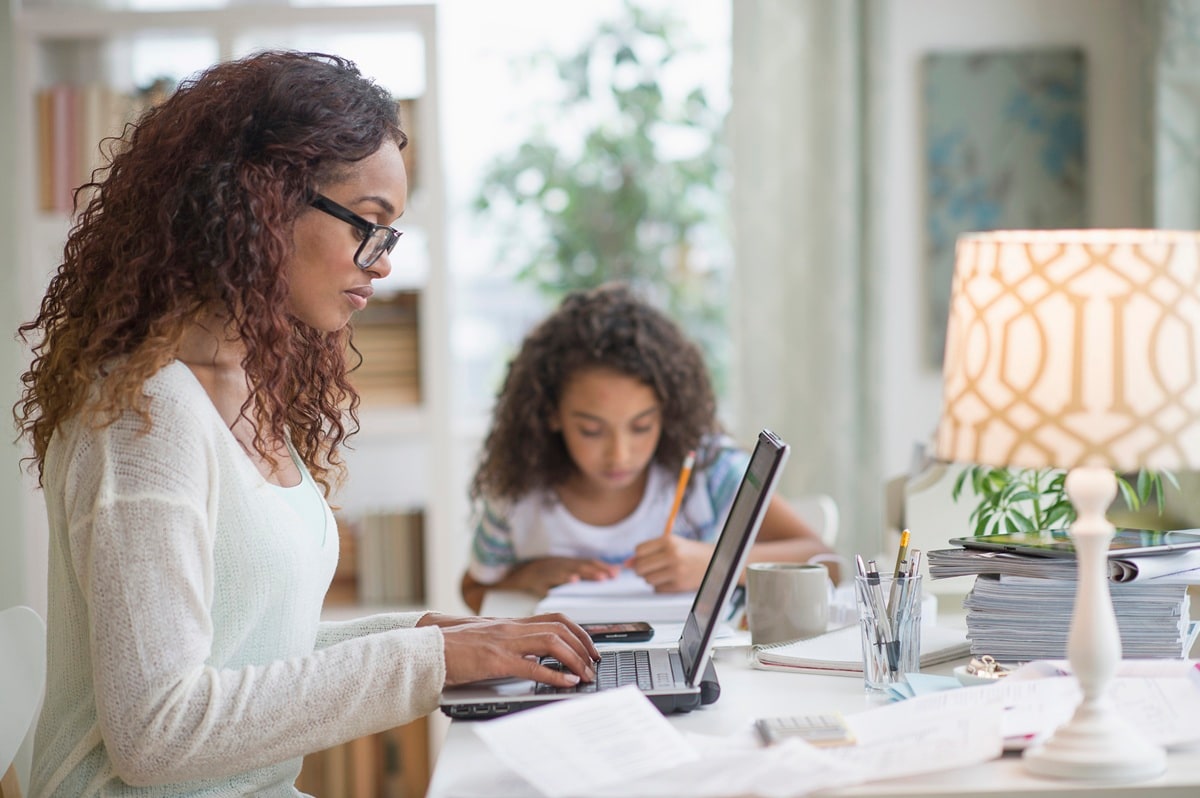 Lady working from home sitting at desk with daughter in background