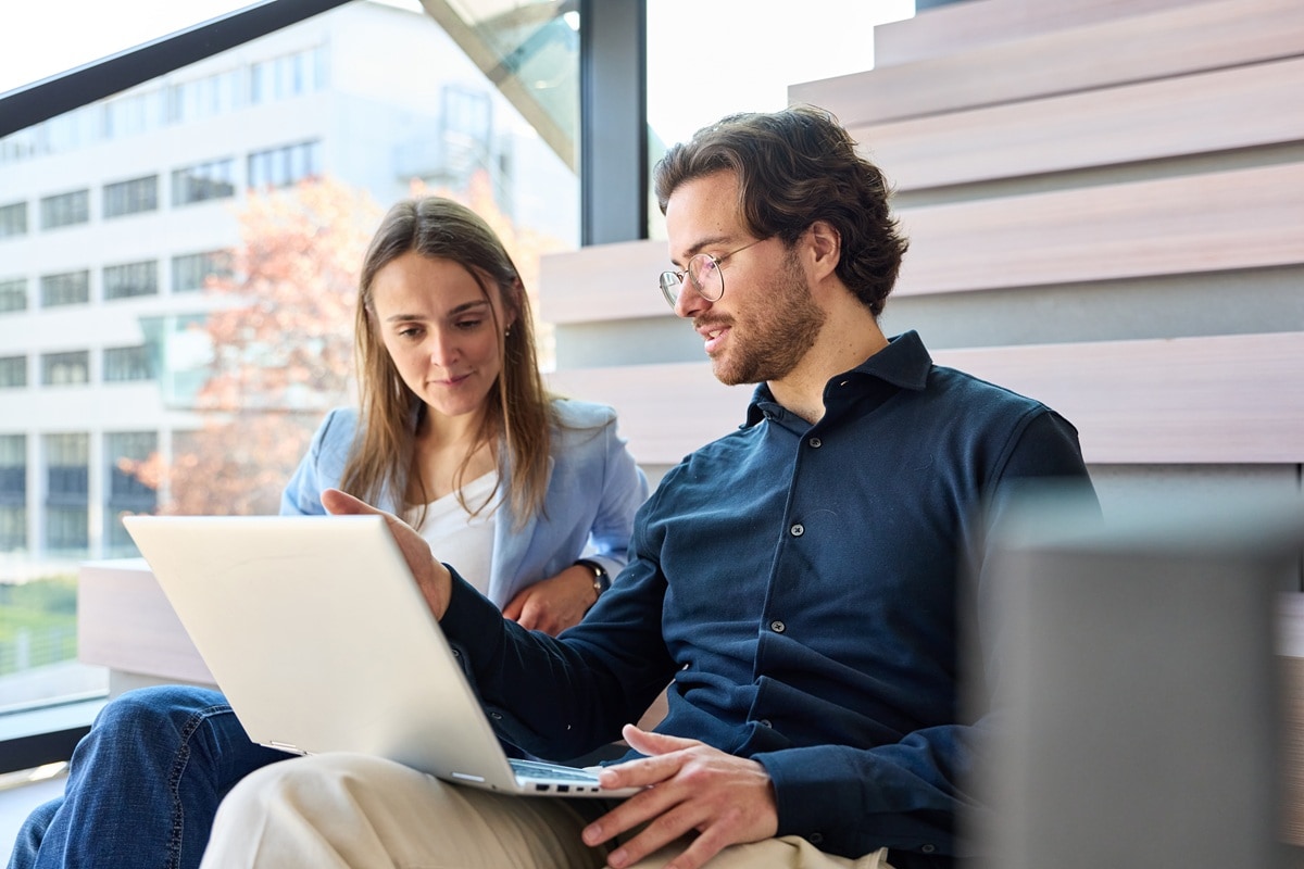 A man and women sitting on sofa in office looking at laptop