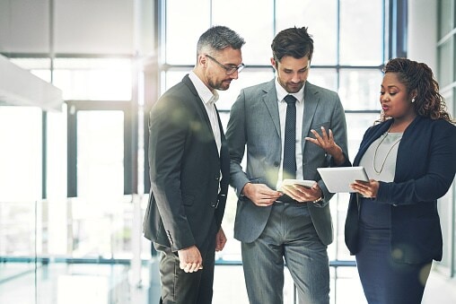 Three people standing in office looking at tablet