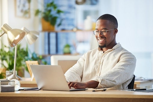 Man in white shirt wearing glasses, sitting at desk working on laptop