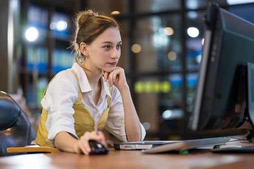Lady in white shirt with waistcoat looking at computer hand on mouse