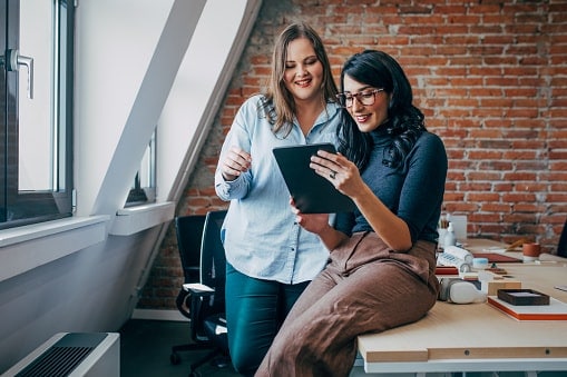 Two ladies sitting on office desk looking at tablet