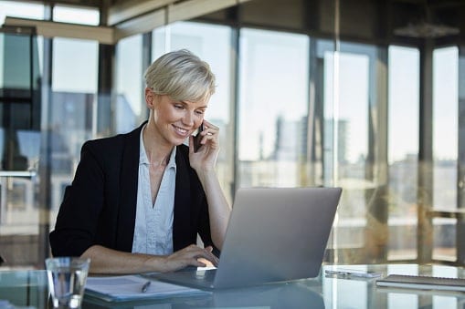 Lady with blonde hair sitting at desk on phone